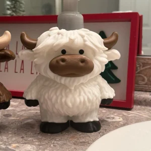 Highland cow soap dispenser holder sitting on a bathroom sink, designed to fit a Bath & Body Works foaming soap bottle, 3D printed farmhouse décor for kitchen or bathroom.