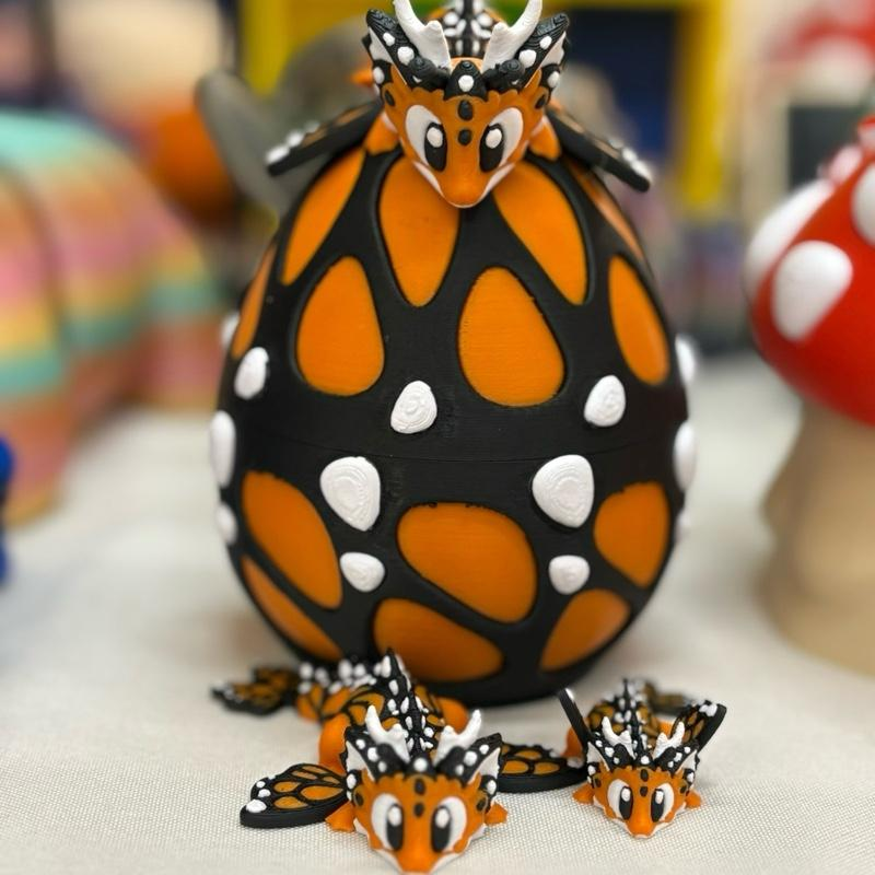 3D printed monarch butterfly dragon set in pink and black featuring three articulated dragons (Daddy, Momma, and Baby) with butterfly wings and a matching decorative dragon egg.