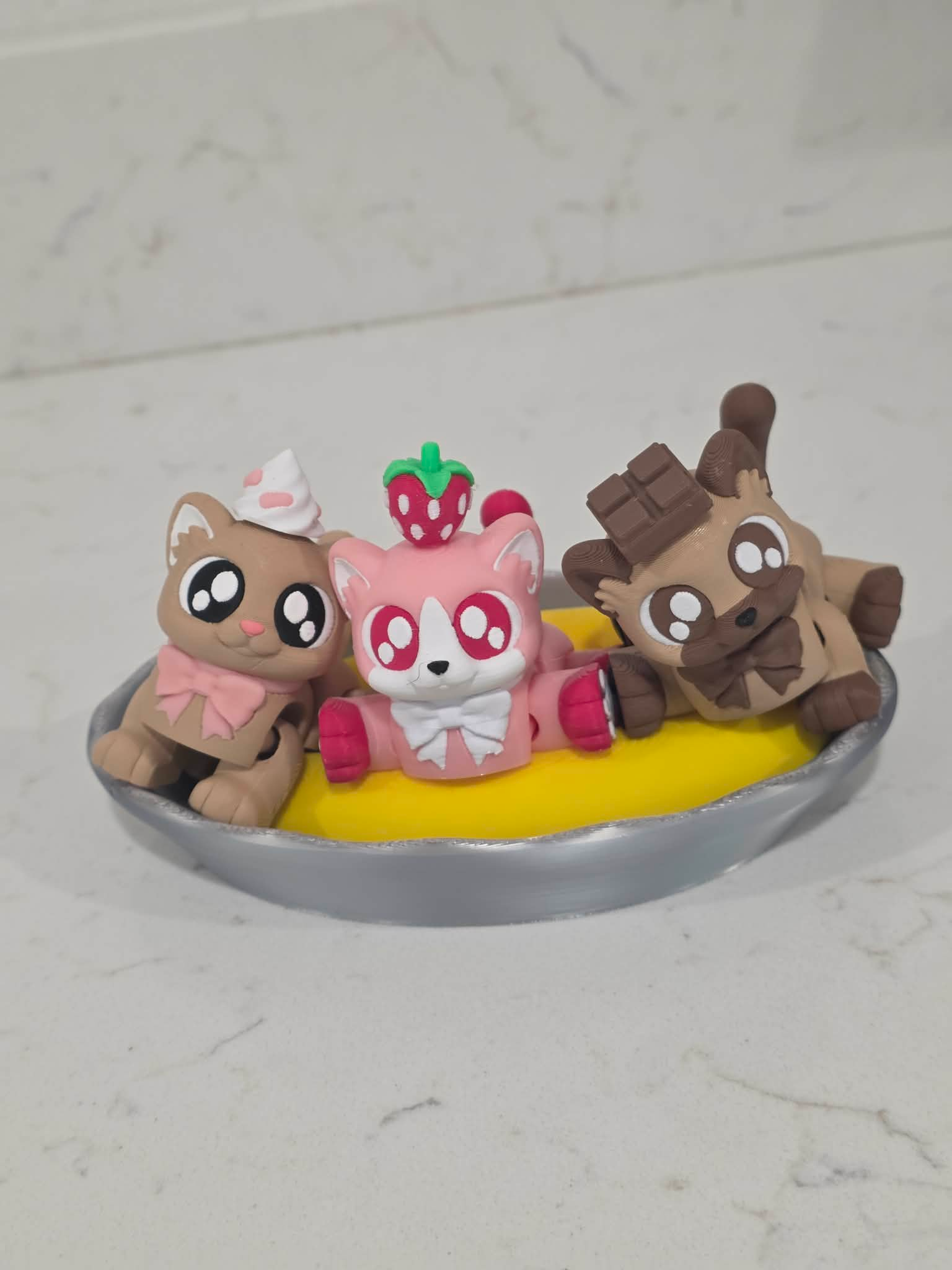 3D printed Banana Splitten Kittens featuring strawberry, vanilla, and chocolate dessert-themed cats sitting in a banana split dish with a sliced banana base, cute collectible cat figures.